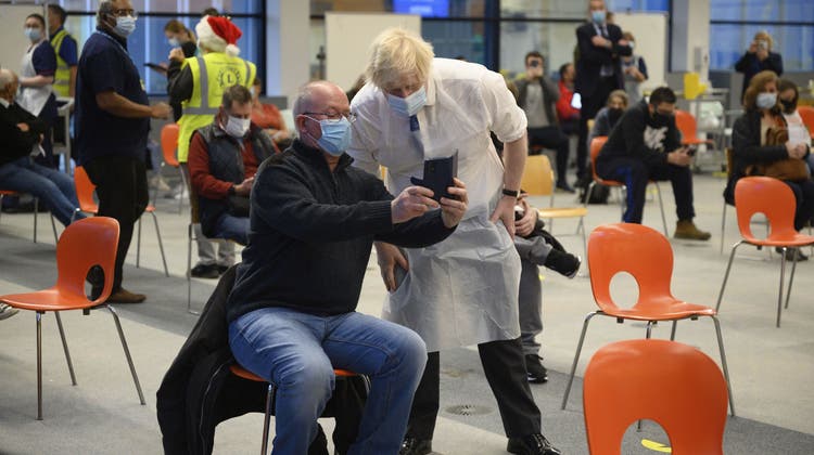 Der britische Premier Boris Johnson (r) posiert beim Besuch eines Impfzentrums in London für ein Selfie. Die Regierung ruft zum Impfen auf, die Omikron-Variante greift auf der Insel um sich. (Leon Neal / AP)