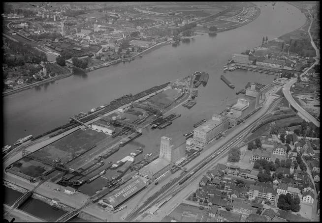 1906 begann in Basel der Bau des Hafens. Das Bild stammt von 1948. Auf der Innenseite des Hafenbeckens I befinden sich die Getreidesilos der führenden Rheinschifffahrtsfirmen. Auf der Aussenseite gegen den Rhein dominiert der damalige Hauptenergieträger, die Kohle.