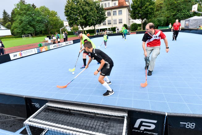 Auf dem blauen Street-Floorball-Feld spielen zahlreiche Teilnehmer in zwei Mannschaften gegeneinander Unihockey.