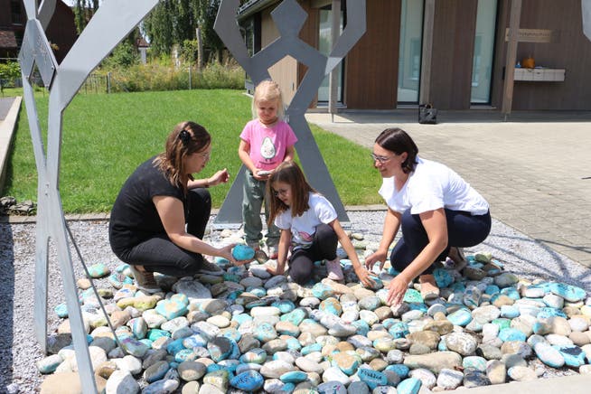 Patricia Jenny und ihre Töchter Zoe und Jael betrachten mit Gemeinde­rätin Maja Brühlmann Zwahlen die bemalten Steine unter der Crea-Statue.