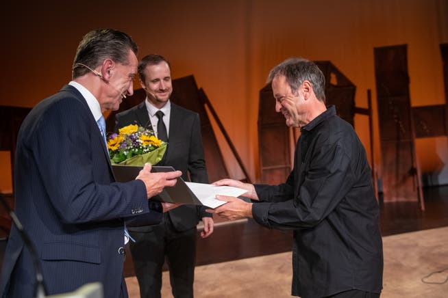 Regierungsrat Beat Jörg (links) überreicht Walter Sigi Arnold den Innerschweizer Kulturpreis 2021. Der Urner Kulturbeauftragte Ralph Aschwanden hält einen Blumenstrauss bereit.
