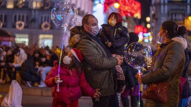 Mit Schutzmaske: eine Familie im weihnachtlich beleuchteten Madrid. (Keystone)
