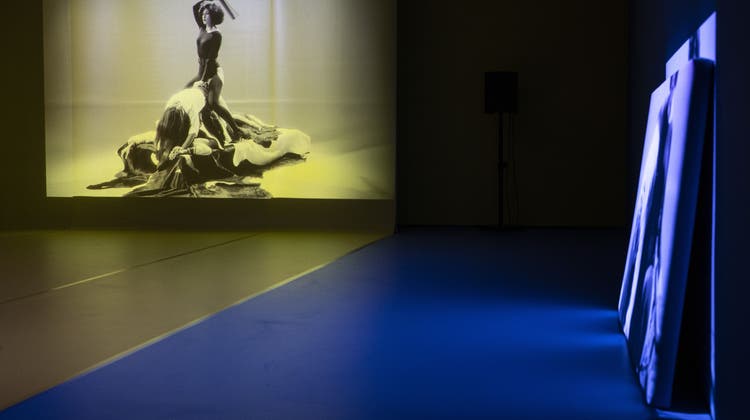 Auf drei Wänden in einem rot-gelb-blau gehaltenen Raum laufen die drei Videoprojektionen von Alexandra Bachzetsis' Werk «2020: Obscene». (Keystone)