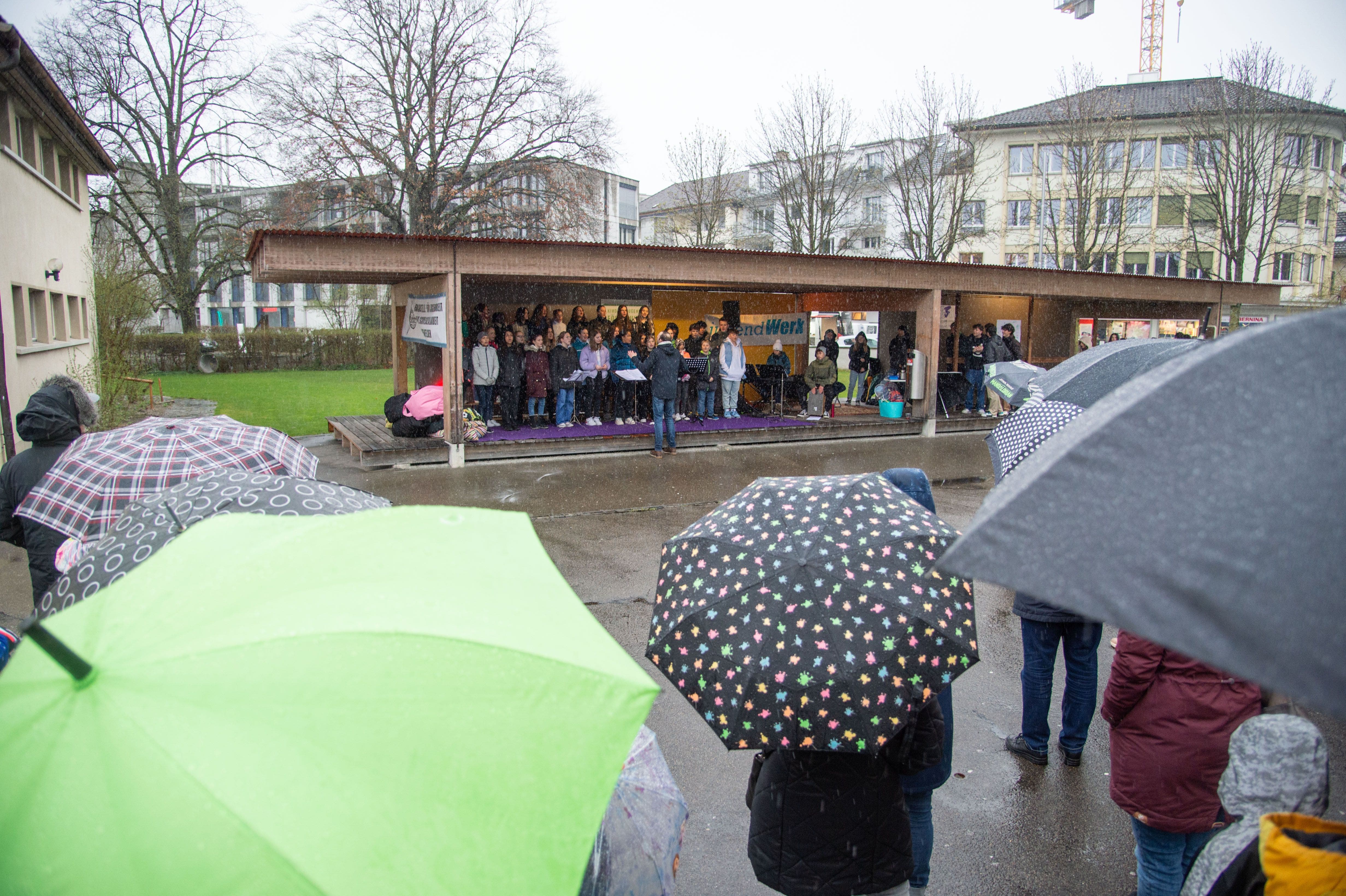 Der Chor der Sekundarschule singt im Pavillon auf dem Schulhausplatz. Viel Publikum unter den Regenschirmen verfolgt den Auftritt.