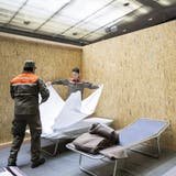 Menschen vom Zivilschutz helfen im Aufbau von Betten und Trennwänden in der Saalsporthalle für die kurzfristige Unterbringung von Geflüchteten aus der Ukraine. (Ennio Leanza / Keystone (Zürich, 22. März 2022))