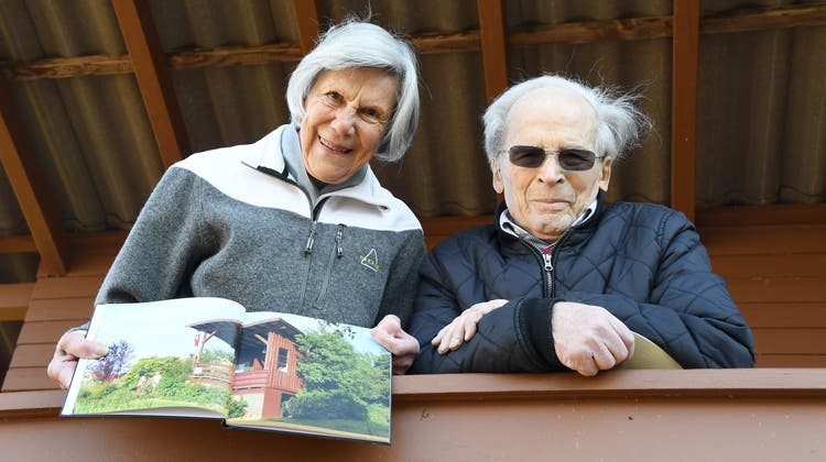 Ruth und Ernst Niklaus stehen auf dem Balkon ihres Freizeithäuschens. Sie zeigen in einem Buch dieses Freizeithäuschen – das einst Wartehäuschen beim Bahnhof Sitterdorf war. (Bild: Yvonne Aldrovandi-Schläpfer)