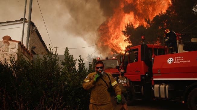 Ein Feuerwehrmann rennt vor den Flammen, die hinter ihm aufsteigen, während eines Waldbrandes in der Vorstadt von Voula.