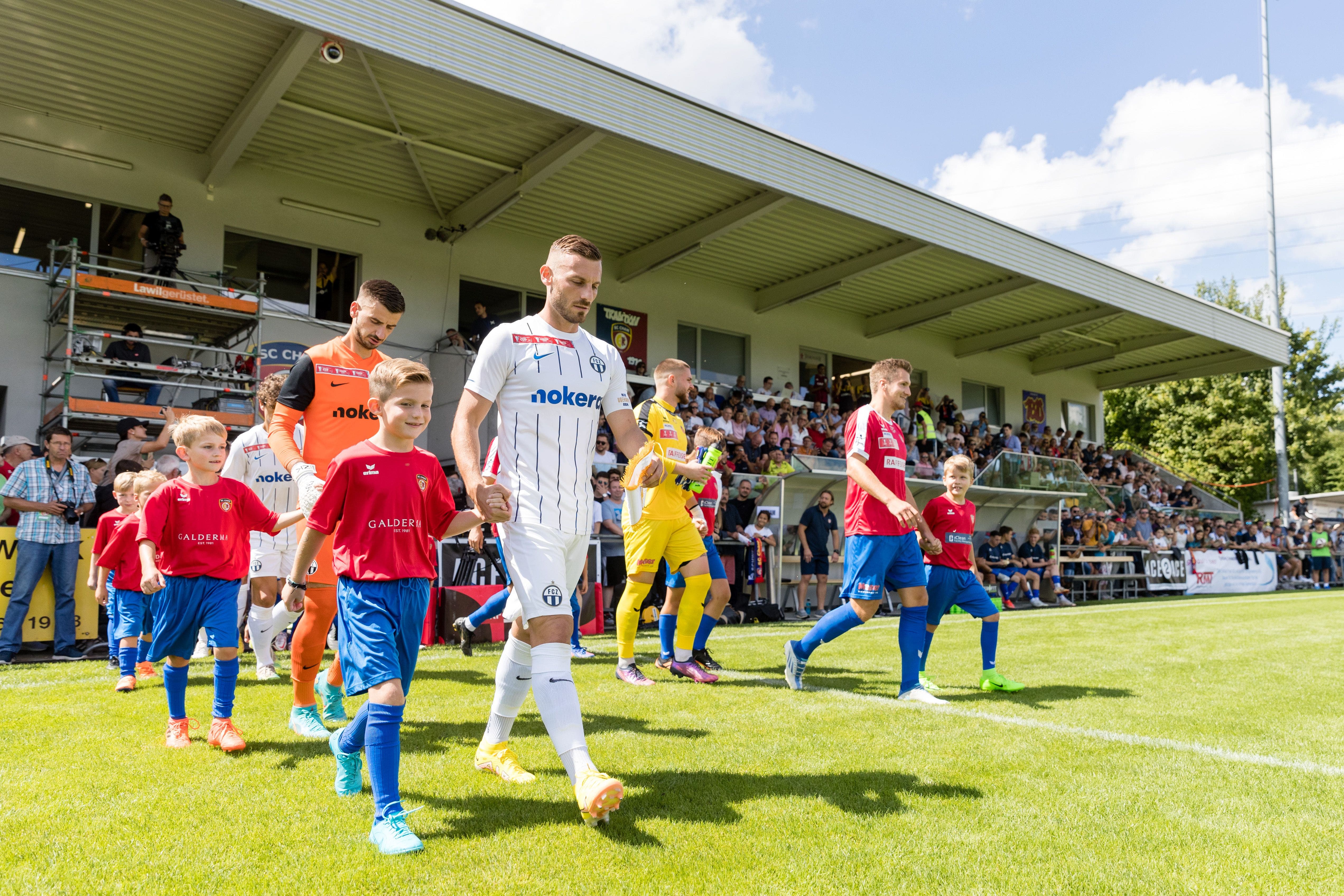 Die Spieler des FC Zürich (links) und des SC Cham betreten das Spielfeld.