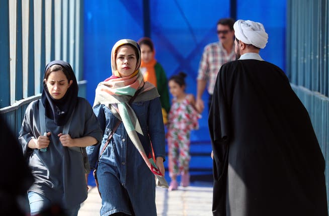 Iranische Frauen laufen in der Hauptstadt Teheran an einem Geistlichen vorbei. Nach dem Tod der 22-jährigen Mahsa Amini brechen Proteste gegen die Sittenwächter im Land aus.