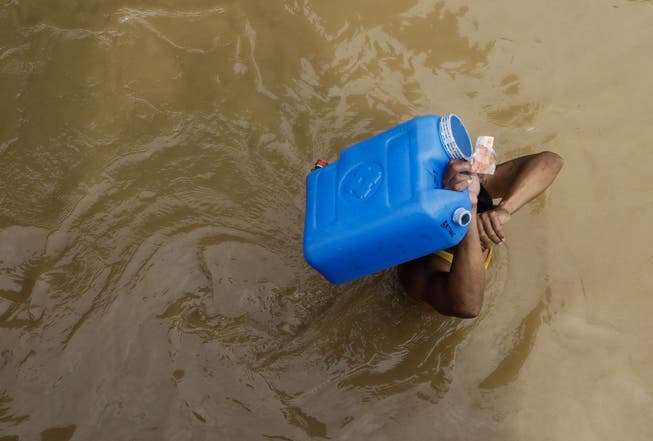 Ein Einwohner trägt einen Wasserbehälter und Geld, während er durch das vom Taifun Noru verursachte Hochwasser in der Stadt San Miguel in der Provinz Bulacan watet. 