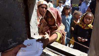 Menschen, die von den Überschwemmungen betroffen sind, erhalten kostenlose Lebensmittel, die von der Pakistan Red Crescent Society in Larkana, Pakistan verteilt werden. (Waqar Hussain / EPA)