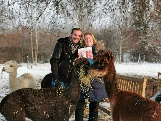 Marc und Desirée Müller mit ihren Alpakas und dem Kinderbuch auf der Weide. 