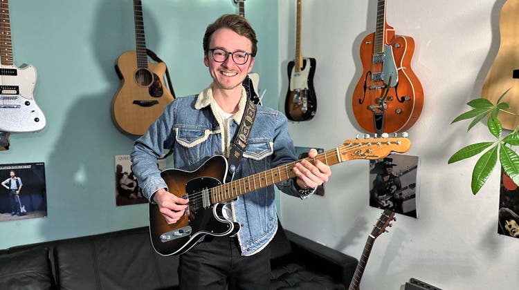 Fabio Nicotera steht in seinem gemütlich eingerichteten Wohnzimmer und präsentiert seine handgefertigte E-Gitarre. (Bild: Felicitas Markoff)