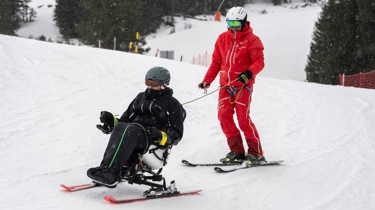 Skilehrer Richard Studer (links) und ein Kollege heben Peter Zihlmann in den Tetraski, ein revolutionäres Gerät für querschnittgelähmte Menschen. (Bild: Dominik Wunderli (Sörenberg, 8. 3. 2023))