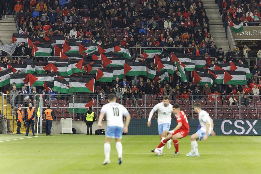 Auf der Tribüne halten Zuschauer aus Protest palästinensische Flaggen in die Höhe.