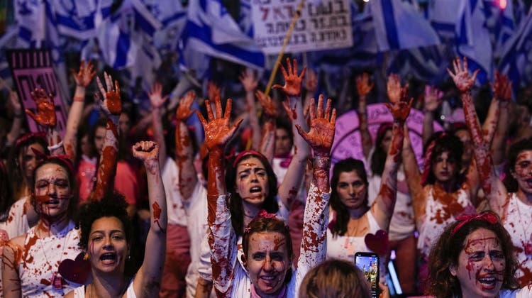 Israelische Aktivisten, die sich mit roter Farbe bespritzt haben, um auf die Gewalt gegen Frauen aufmerksam zu machen, nehmen an einem Protest gegen die Pläne der Regierung von Premierminister Benjamin Netanjahu zur Überarbeitung des Justizsystems in Tel Aviv (Bild: Ariel Schalit / AP)