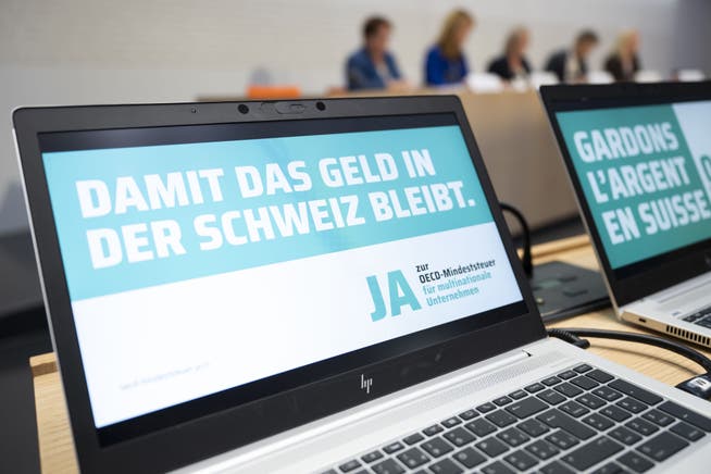Der Slogan «Damit das Geld in der Schweiz bleibt» erscheint auf einem Bildschirm, an einer Medienkonferenz der Allianz für die Umsetzung der OECD-Mindeststeuer.