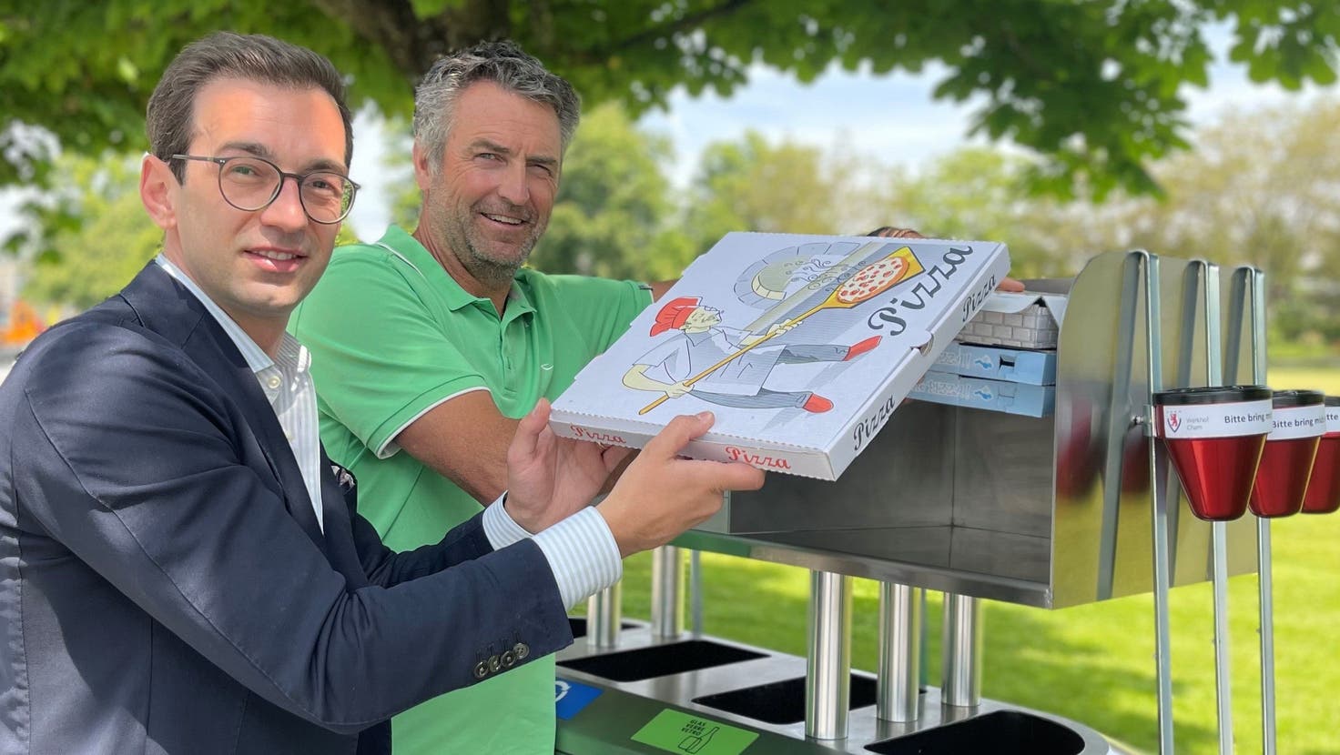 Gemeinderat Drin Alaj (links) und Roger von Ah, Bereichsleiter Werkhof, weihen den brandneuen Pizzakarton-Aufsatz auf der Recyclingstation im Chamer Hirsgarten ein. (Bild: PD/Gemeinde Cham)