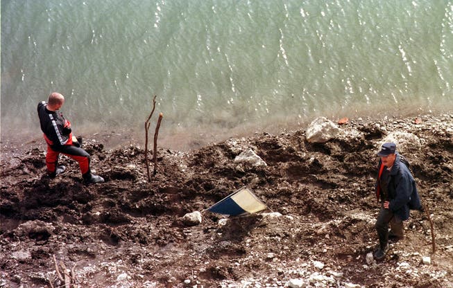 Polizisten suchen den Fundort ab: An der markierten Stelle lag das weisse, darunter im Wasser das orange Fass mit je einer Leiche. 