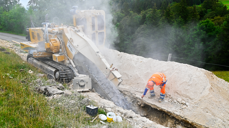 Die Grabenfräsmaschine frisst sich durch den Fels, ein Mitarbeiter misst die Grabentiefe. (Bild: Oliver Menge)