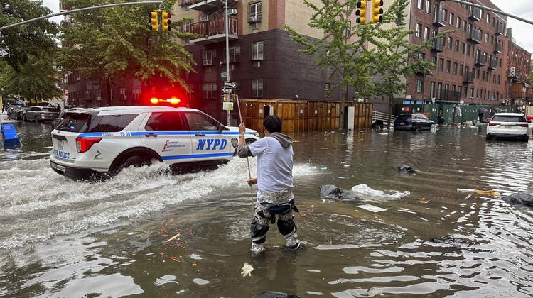 Fast knietief steht ein Mann mitten auf einer New Yorker Strasse im Wasser, auch die Polizei kommt mit ihrem Auto nur langsam voran. (Bild: AP)